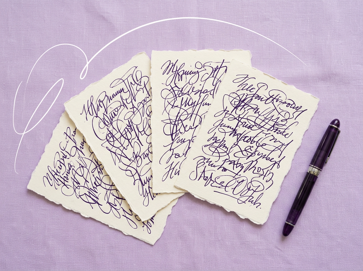 Four cream deckle-edge cards covered in purple ink handwriting, fanned out beside a fountain pen on lilac fabric